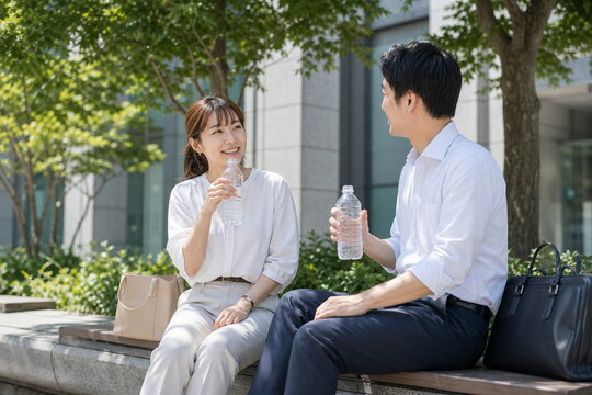 夏の昼休みに日陰で水を飲む会社員