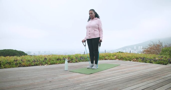 Fog coaxing Senior African American woman wearing pink jacket doing band curls on deck keeping fit