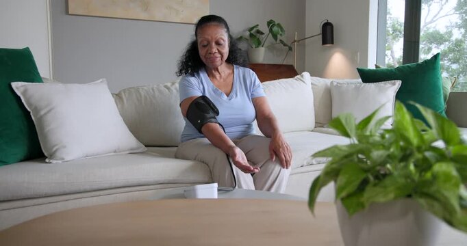 African American senior woman preparing to check BP at home, adjusting cuff, checking device