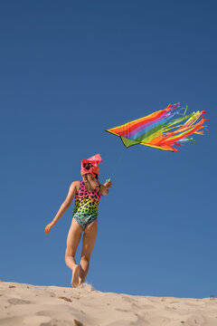 A child launches a rainbow kite. A girl in a swimsuit against a clear blue sky. Rear view
