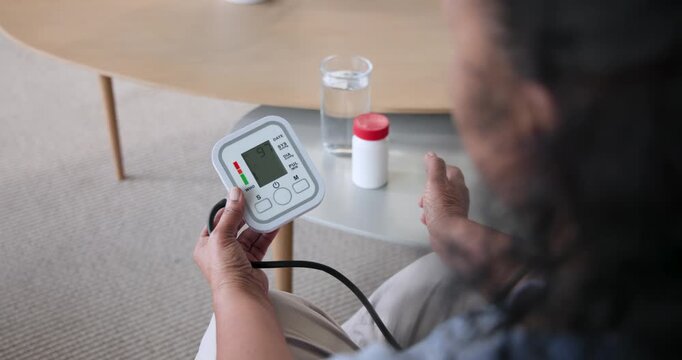 Senior African American woman sitting at home using BP monitor after pill bottle, copy space