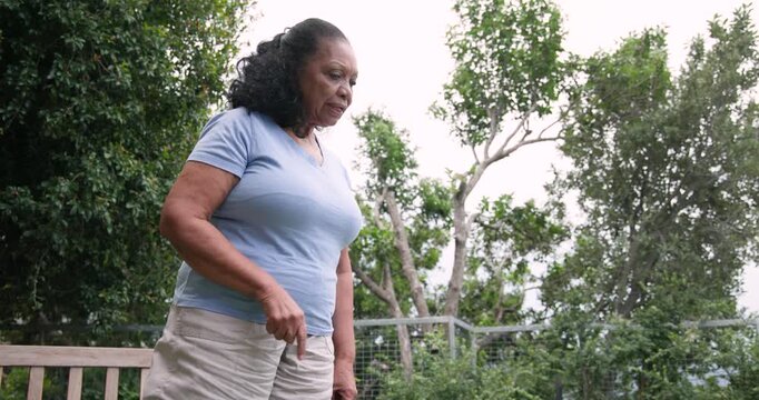 Senior African American woman entering left, walking, pointing, chiding offscreen at backyard bench