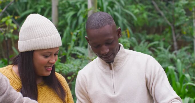 African American couple inspecting seedlings, planting them in garden planter using trowel