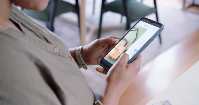 Woman wearing khaki shirt sitting in cafe holding card, scrolling phone, weighing Black Friday deal