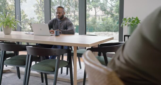 African couple woman rising from counter scrolling phone, revealing man typing for work on laptop