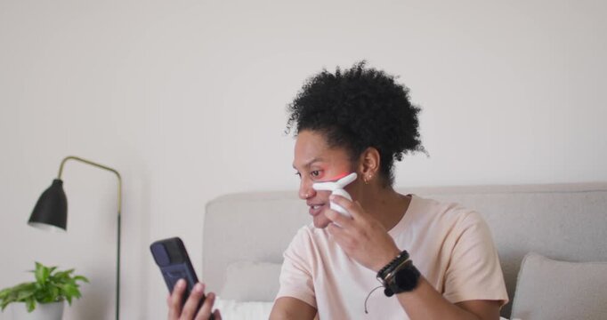 African American woman on bed holding phone following app while moving Tshaped device along jawline