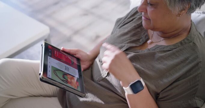 Senior woman wearing olive blouse scrolling tablet in living room, touching necklace after prompt