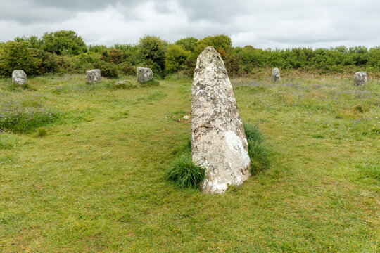View of the Boscawen-un Stone Circle with a large central standing stone surrounded by smaller megaliths in a grassy field under a cloudy sky in Penzance, England, United Kingdom.