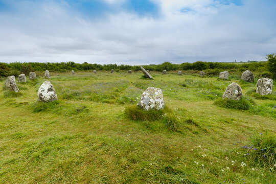 View of ancient Boscawen-un Stone Circle with weathered standing stones and a central leaning monolith in a lush green field under a cloudy sky Penzance, England, United Kingdom.