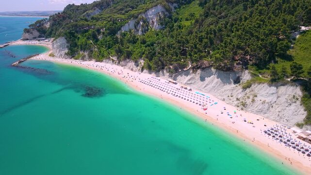 Sirolo Marche Italy 4k drone of San Michele beach and Urbani. Top-down aerial reveal of turquoise sea water moving to medieval village resort on cliff toward Monte Conero mountain summer b-roll