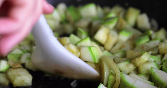 Cooking and stirring stewed zucchini with onions in ghee in a frying pan
