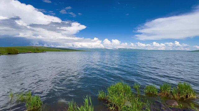 Cinematic panning shot of the scenic Lake &Ccedil;ıldır (&Ccedil;ıldır G&ouml;l&uuml;) during spring, featuring lush green shores, distant snow-capped mountains, and dramatic clouds
