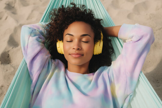 Top view of peaceful young woman resting in a hammock on the beach wearing yellow headphones