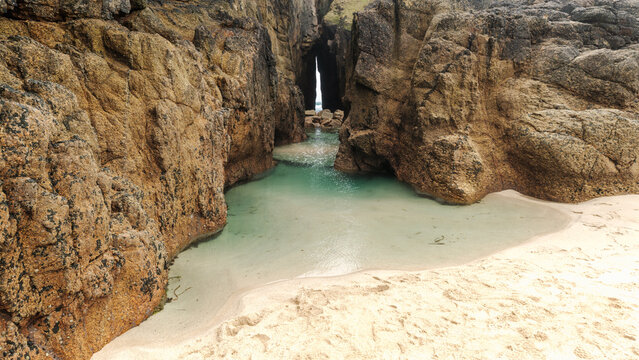 View of the Song of the Sea rock arch and turquoise tidal pools at Nanjizal Bay with rugged granite cliffs and white sand Saint Just, England, United Kingdom.