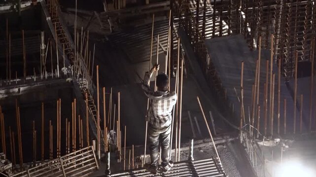 Delhi, India - 12th Mar'26: Construction worker assembling reinforced concrete structures at a building site during nighttime, illuminated by floodlights showing labor without safety