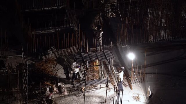 Delhi, India - 12th Mar'26: Construction workers assembling reinforced concrete structures at a building site during nighttime, illuminated by floodlights showing labor without safety