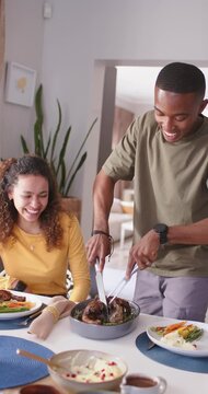 Vertical video: Couple watching man placing fork, carving roast with knife at home preparing meal