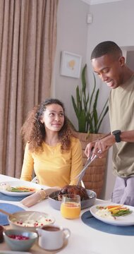 Vertical video: Couple watching man bringing roast, carving with fork knife at table for dinner