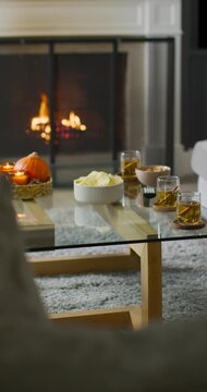 Vertical video: Glass table holding chips and drinks near fireplace flames flickering, casting glow