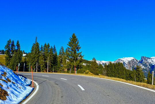 Bergfahrt auf der Jaunpassstrasse mit Schneeresten auf den Bergwiesen unter strahlend blauem Himmel