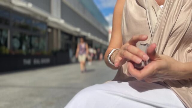 Hands of a young female shuffling cards outside in the sunlight with space for text as people in the blurred background walk past