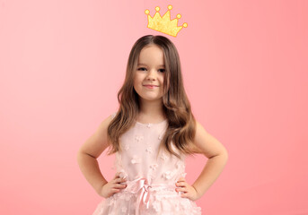 Cute little girl with crown above her head dreaming to be queen. Pink background