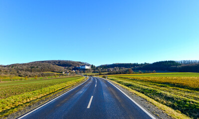 Fototapeta premium Fahrt auf einer geschwungenen Landstraße im Grabfeld mit Blick auf das Schloss Sternberg; Bayern 