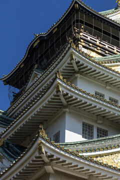 View of the ornate rooftops of Osaka Castle featuring traditional green tiles and gold ornaments against a clear blue sky in Osaka, Osaka, Japan.