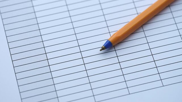 An orange ballpoint pen lying on a blank paper table grid document. Close up.