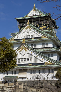 View of the historic Osaka Castle featuring its iconic white walls and green roofs with gold ornaments under a clear blue sky in Osaka, Osaka, Japan.