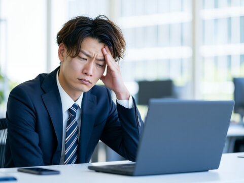 仕事のストレスで疲労困憊する若い日本人男性がパソコンを見つめる