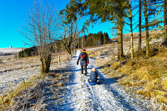 Mutter zieht ihr Kind auf dem Schlitten bei einer Winterwanderung auf der Wasserkuppe in der Rh&ouml;n, Hessen