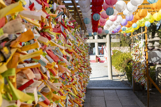 View of vibrant colorful prayer strips and rows of paper lanterns hanging along a stone path at a traditional shrine in Osaka, Osaka, Japan.