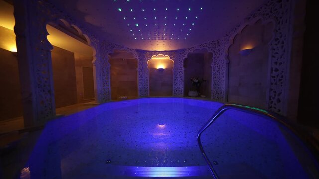 Moroccan inspired hammam shows scalloped arches, filigree panels, and a mosaic plunge pool in deep blue, with gentle ripples and subtle reflections on the handrail.