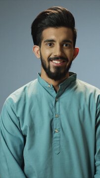 Friendly close up portrait of handsome man wearing traditional shirt and smiling gently at camera. Arabian male standing relaxed and showing positive mood. Indoor simple lifestyle scene.