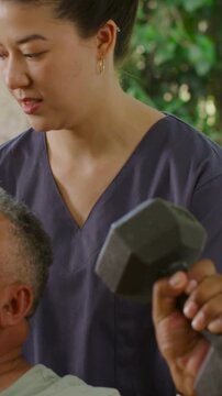 Vertical video: Supporting therapist in scrubs steadying patient starting hex dumbbell press patio