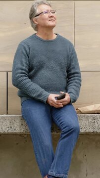 Vertical video: Reading phone man in teal sweater adjusting grip in lobby, glancing at paper bag