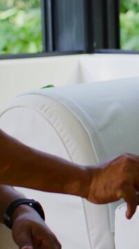 Vertical video: Leaning man in shirt, watch reaching over sofa fixing pillow by window, copy space