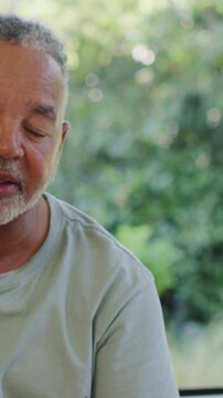 Vertical video: Framing shifting as mature man speaking, turning by window bokeh, wearing sage tee