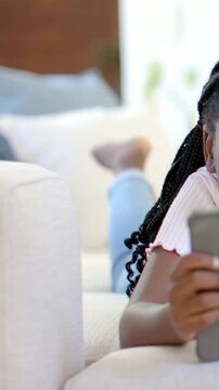 Vertical video: Cam pulling back kid holding tablet focusing, lying on sofa in pink top, copy space