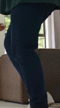 Vertical video: Right foot lifting one in green top, shoes stepping on couch by window bracing