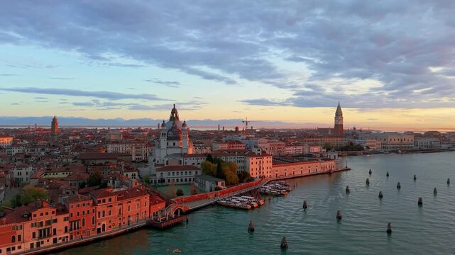 Venice aerial sunset over lagoon, boats gliding past basilica santa maria della salute, pastel sky casting. Italy