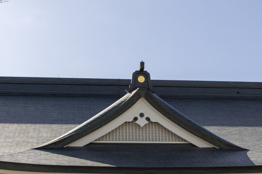 View of a traditional Japanese temple roof featuring a decorative gable and gold emblem against a clear blue sky Osaka, Osaka, Japan.