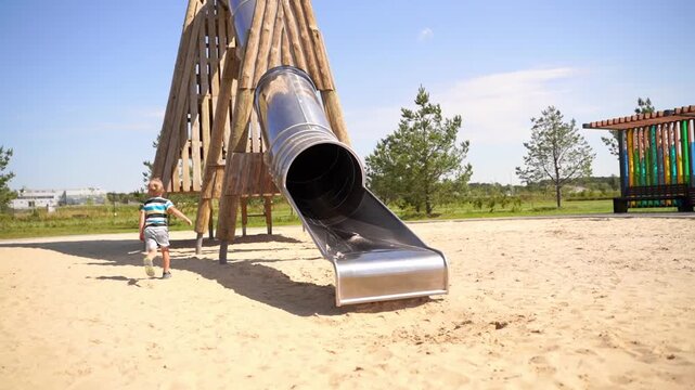 child, playground, slide, fun, summer, sand, happiness, entertainment, physical activity, family time, fresh air,  laughter, growth, development, positive emotions, trees, blue sky, wooden structure, 