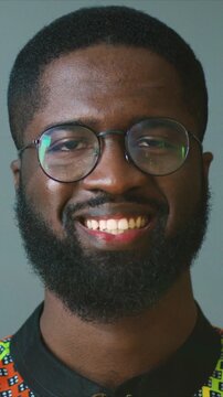 Close up portrait of African American man wearing glasses and patterned traditional shirt. Cheerful young male looking at camera and smiling. Indoor cultural lifestyle scene. Joyful mood concept.