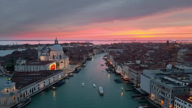 Venice aerial sunset over lagoon, boats gliding past basilica santa maria della salute, pastel sky casting. Italy