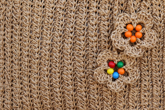 Close-up of a woven raffia background with handmade crochet flowers and colorful beads.