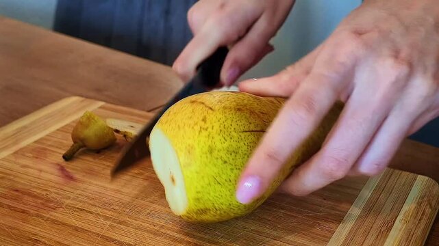 Close-up: slicing a pear into thin pieces with a kitchen knife on a cutting board.