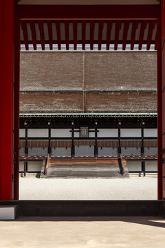 View of the traditional architecture of the Kyoto Imperial Palace with its large thatched roof and white walls seen through a red gate in Kyoto, Kyoto, Japan.