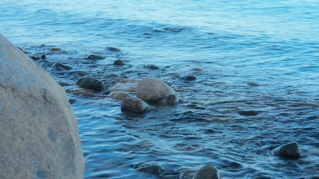 Gentle blue ocean waves washing over rocks on a peaceful stony beach